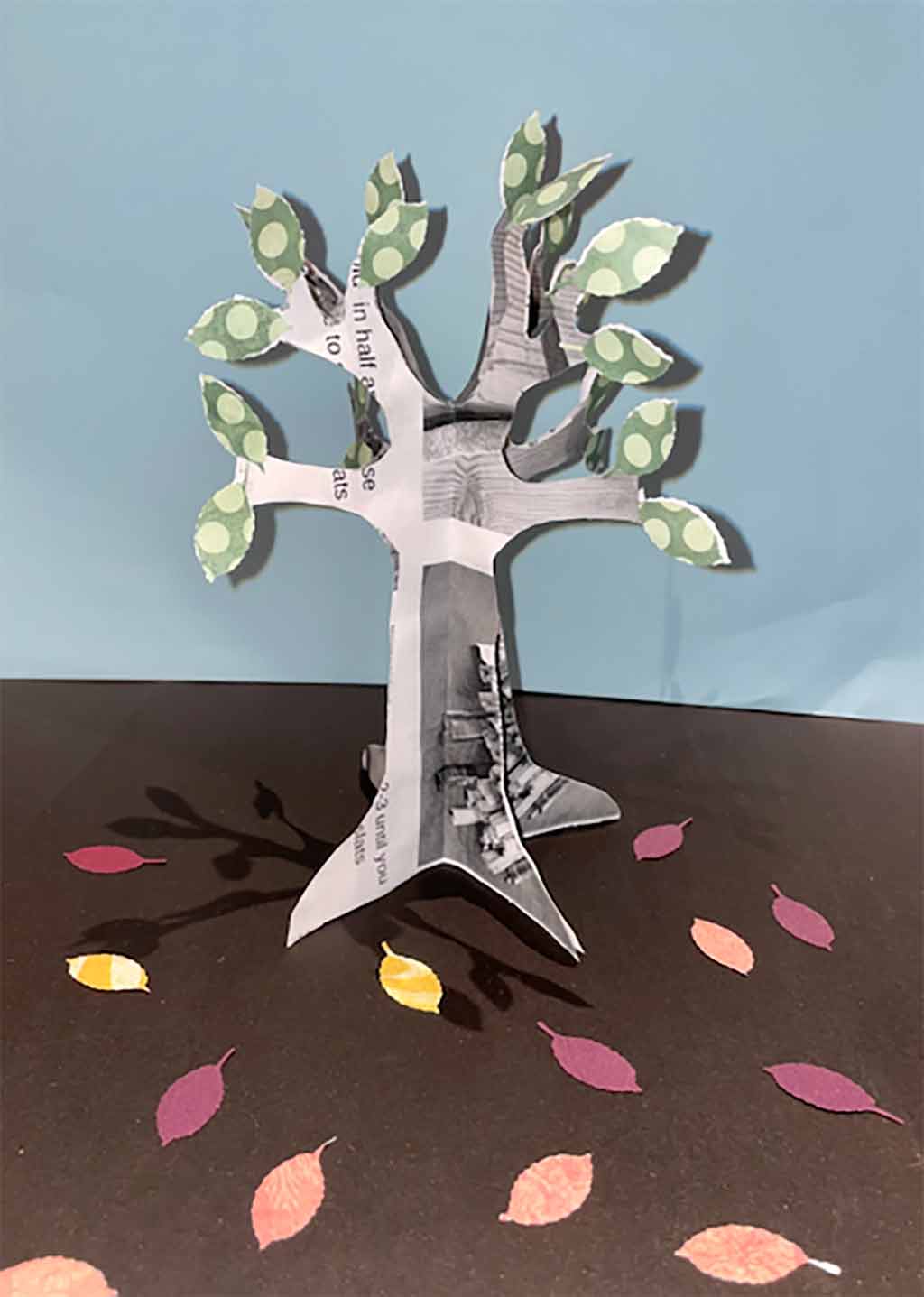 paper craft tree with green leaves placed on a table with paper leaves of fall colors
