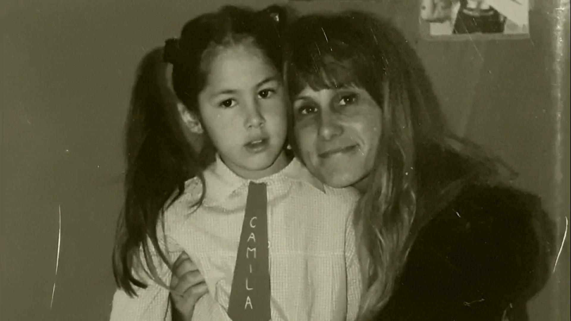 A mother holding her daughter who is wearing a tie that reads, 'Camila' 