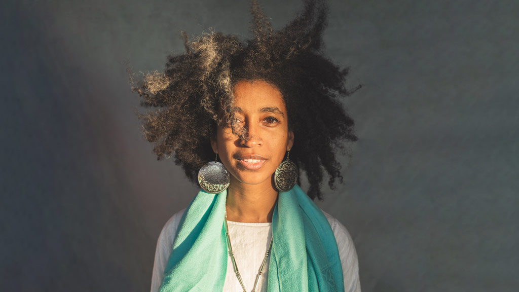 a woman wearing large disk earrings and a turquoise scarf in front of a plain gray background