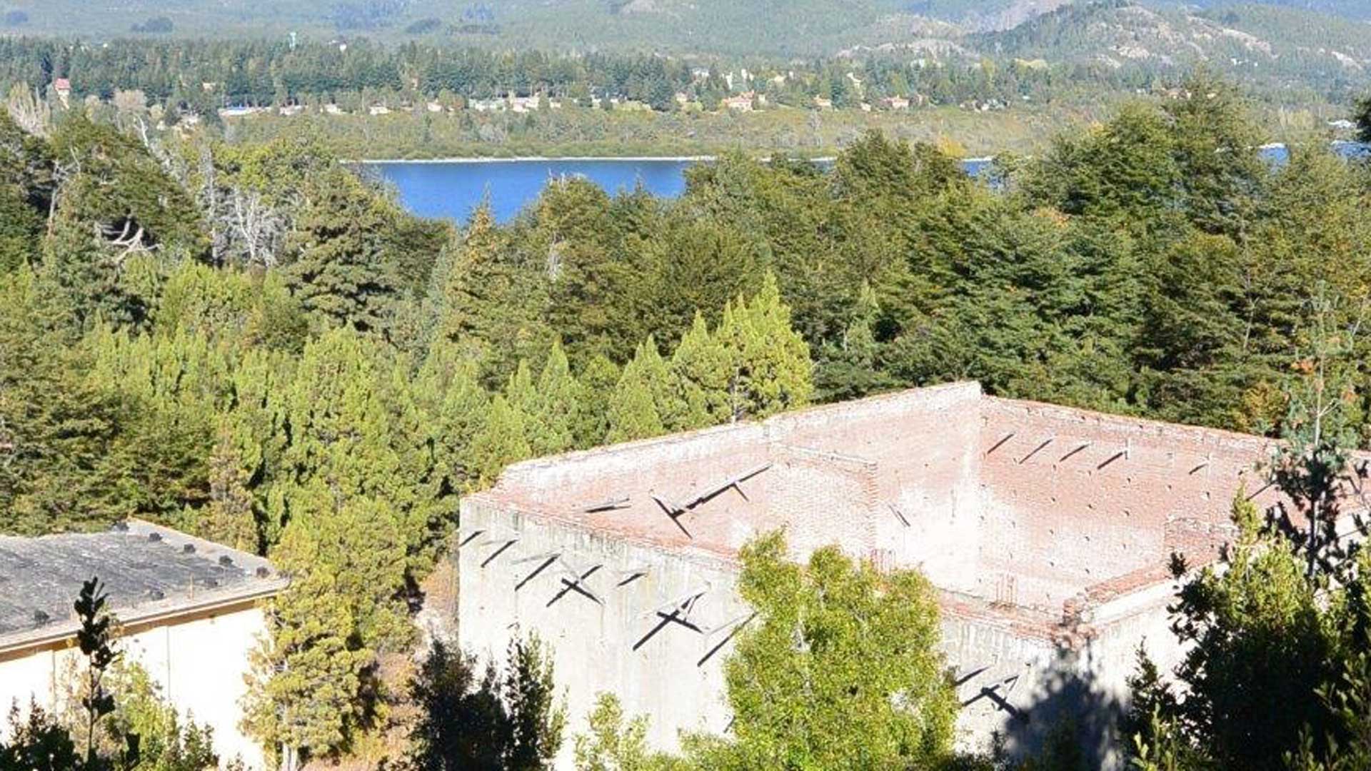 old brick structure surrounded by trees, with a lake and mountains in the background