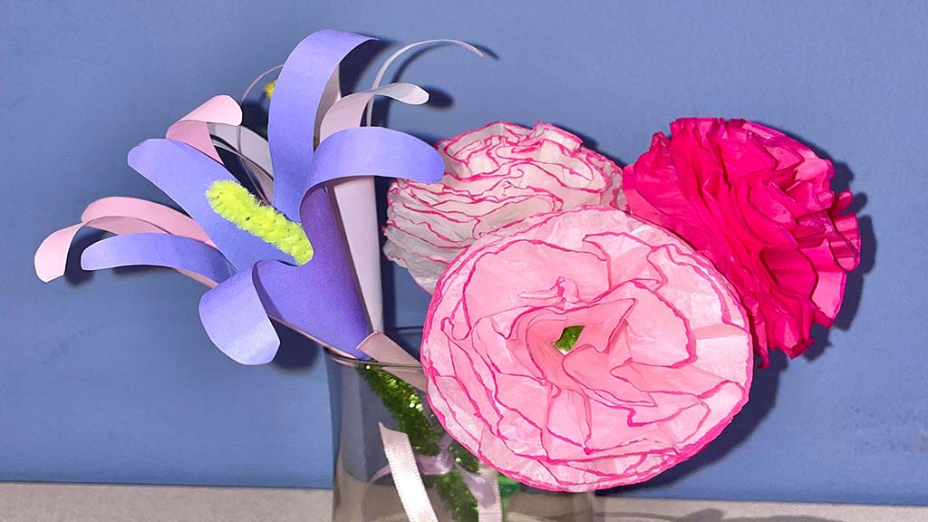 pink and purple flowers made out of cut paper sitting in a glass cup