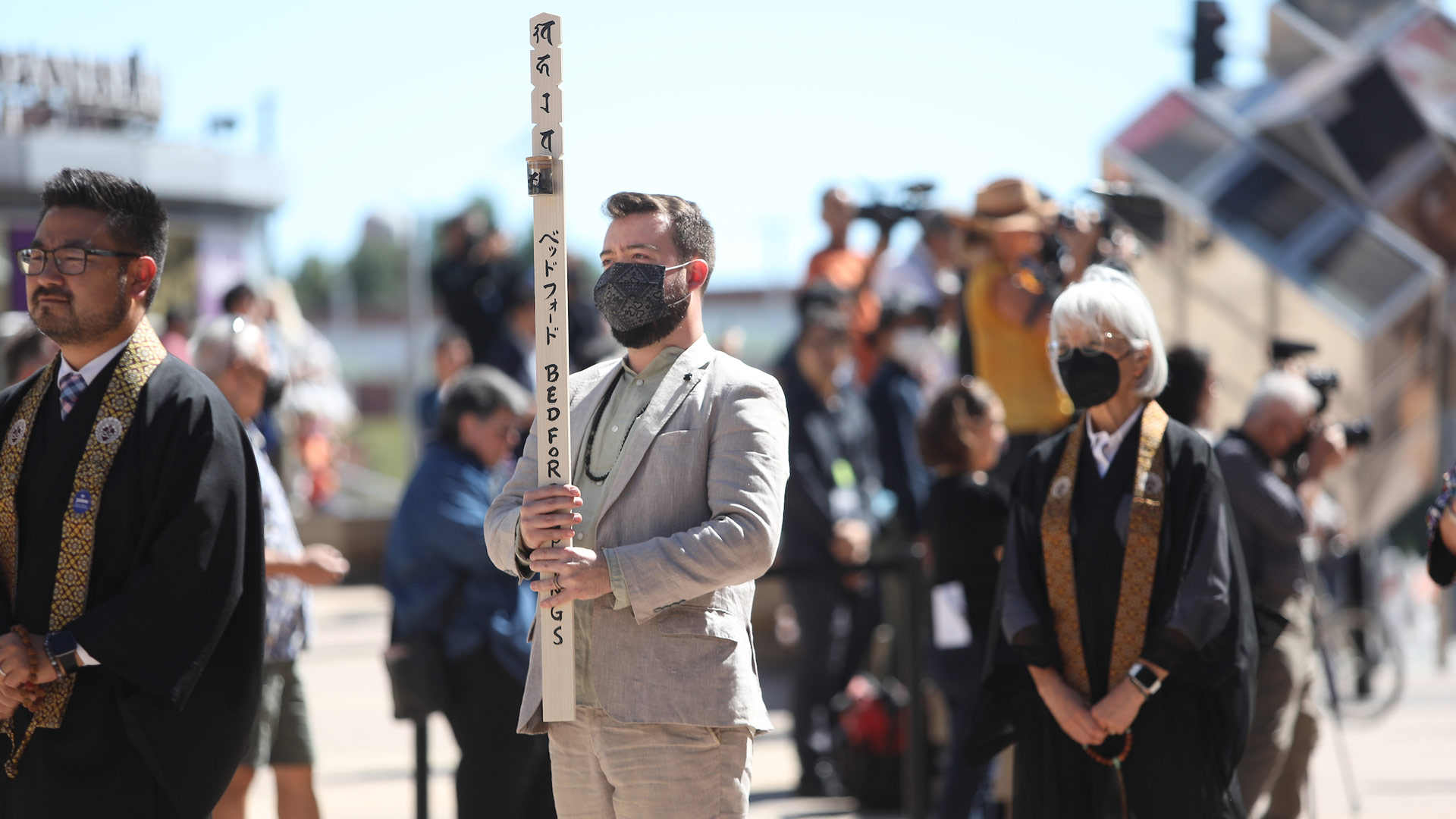 Man wearing a mask holding a wooden pole with an inscription