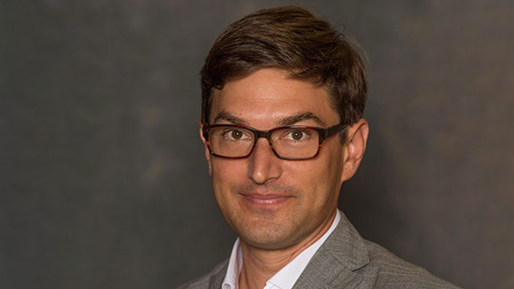 portrait of a main with glasses wearing a suit on a gray background
