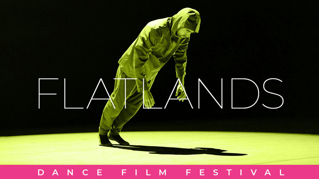 man in a hooded jacket and sweatpants leaning forward and casting a harsh shadow on an empty green floor