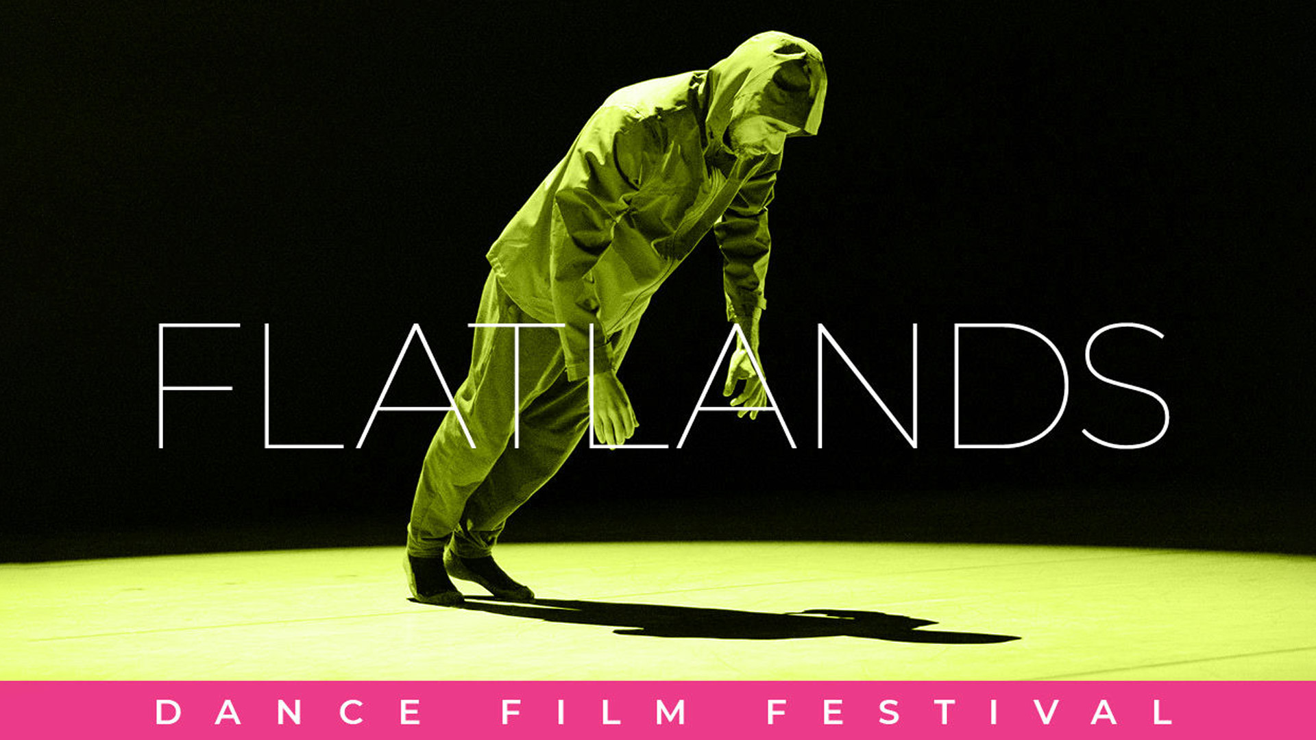 man in a hooded jacket and sweatpants leaning forward and casting a harsh shadow on an empty green floor