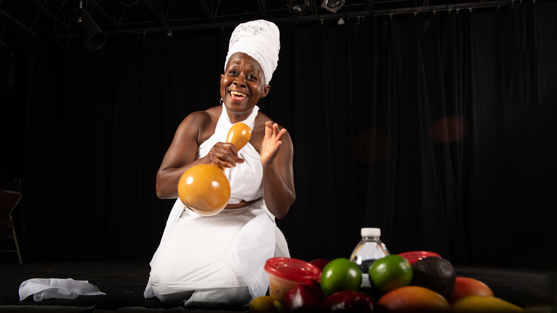 African woman holding a wooden instrument with a bowl of fruits in the foreground