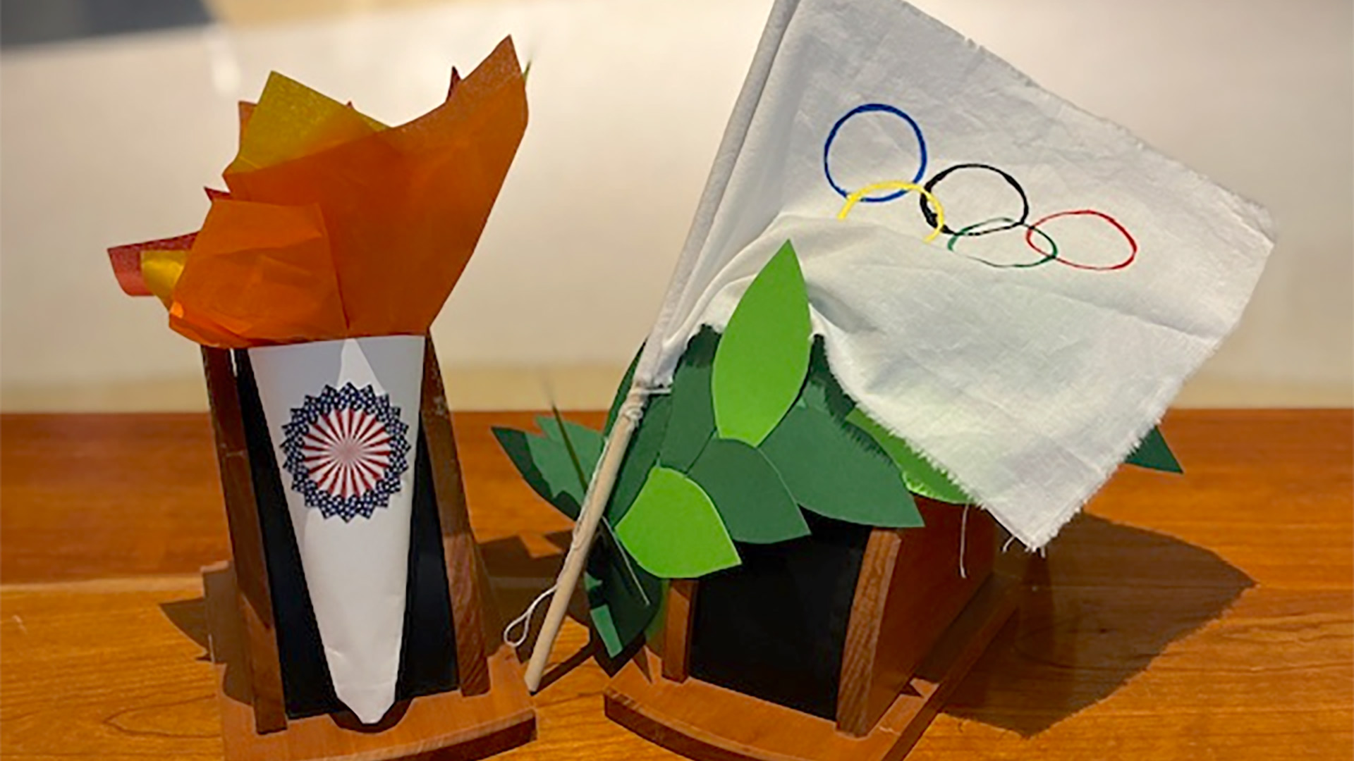 A paper craft imitation of the olympic torch, white flag, and a green leaf crown