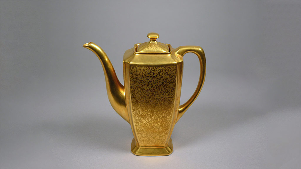 A shiny golden tall pitcher with knobbed lid, and long spout and handle