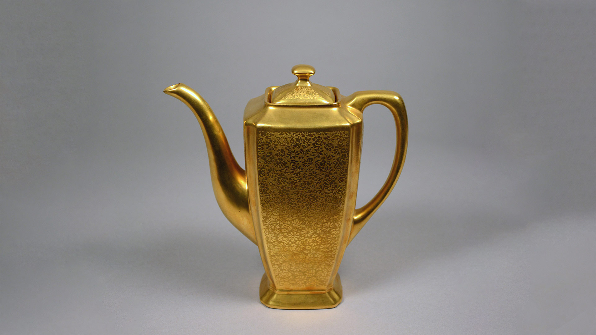 A shiny golden tall pitcher with knobbed lid, and long spout and handle