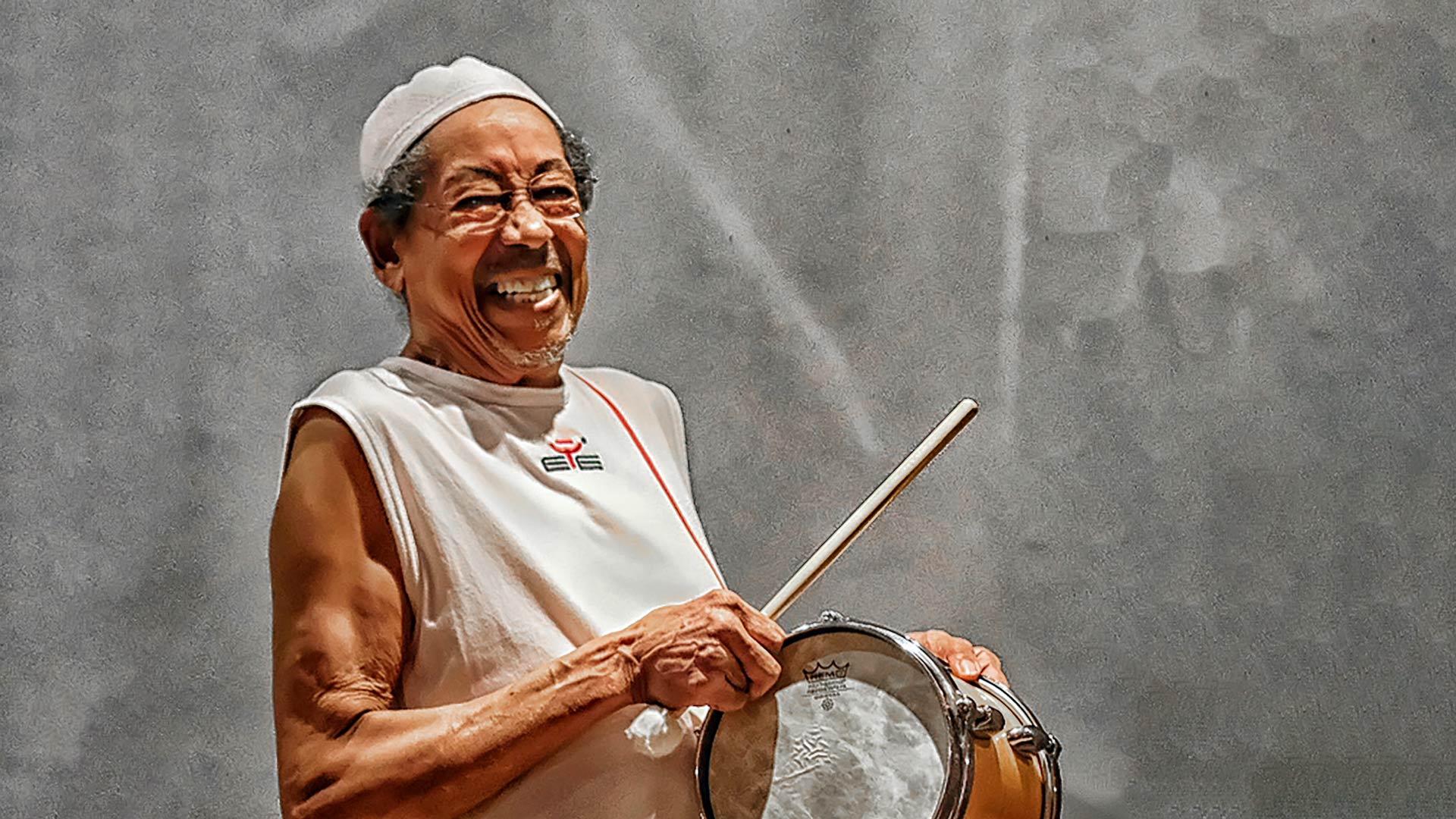 Older man smiley widely and holding a drum and drumstick