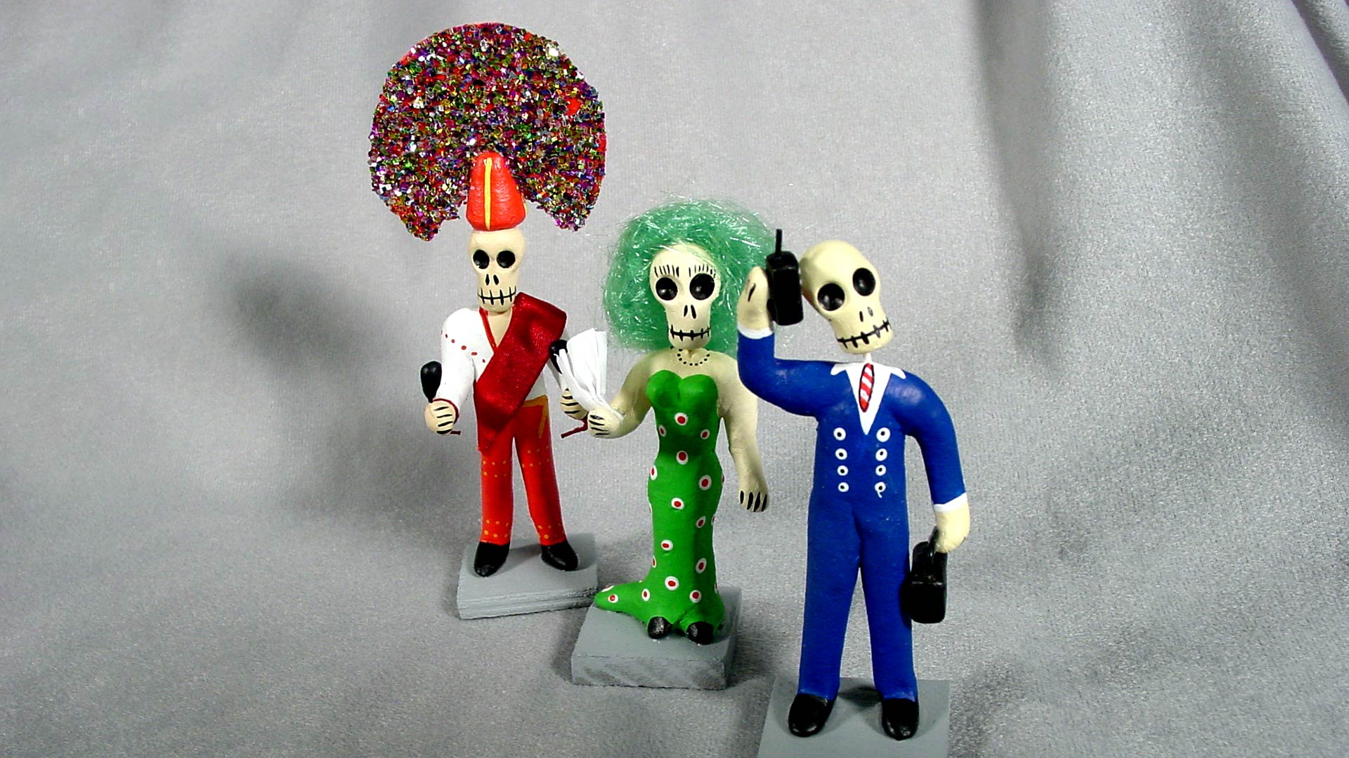 3 small table decorations, including 3 skeletons dressed like living people with microphone, dress, and cellphone