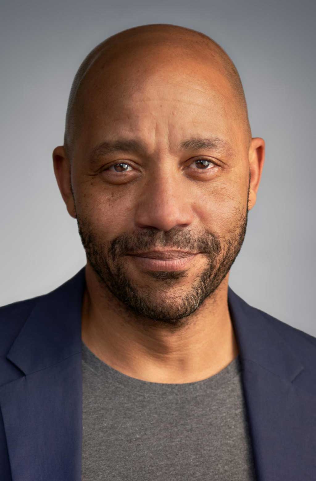 a head shot of a man in a dark blue blazer looking straight with a smile.