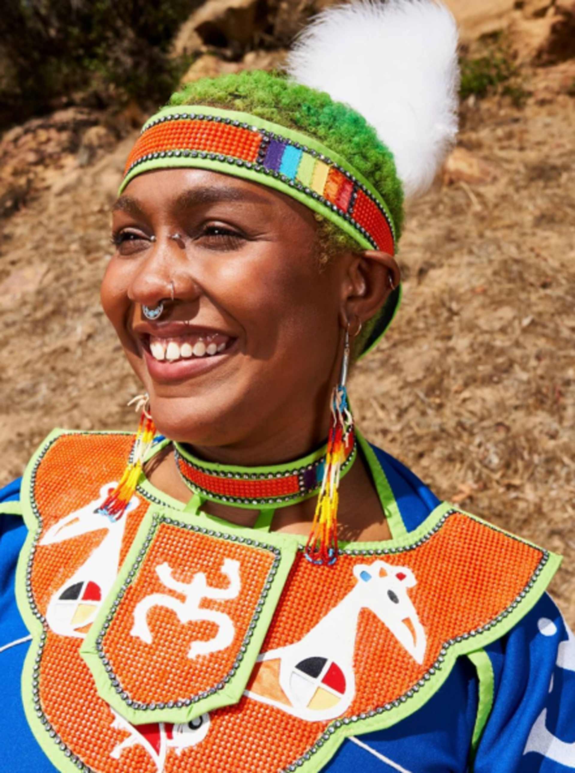 Indigenous person with green hair wearing colorful traditional clothing and headband