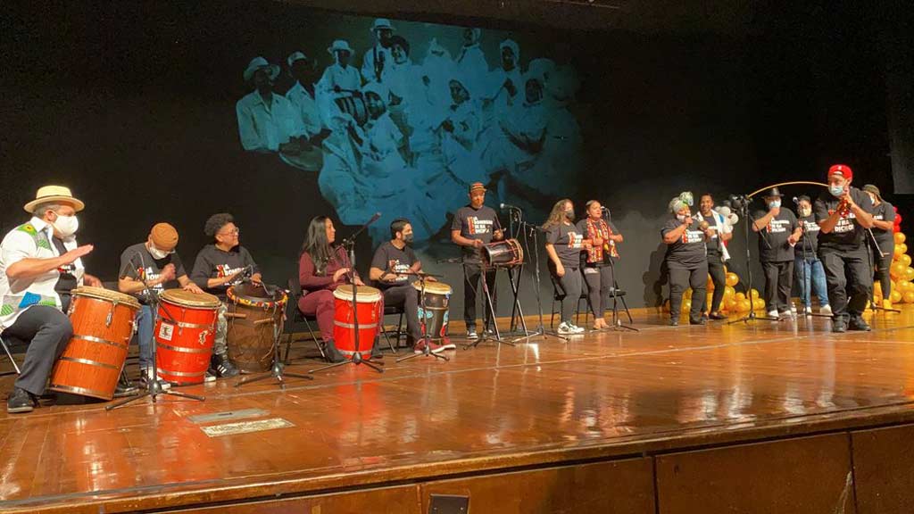 A line of drummers and singers on stage.