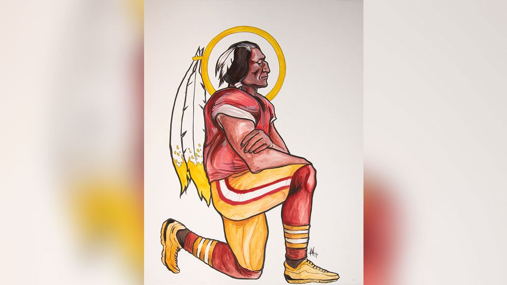 a man in a football uniform with feathers attached to his hair taking a knee.