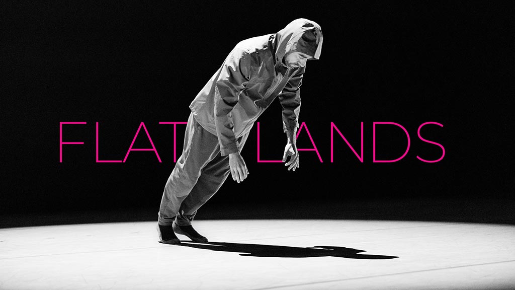 dancer wearing a hooded jacket and pants leaning forward over a spotlight in front of FLATLANDS text