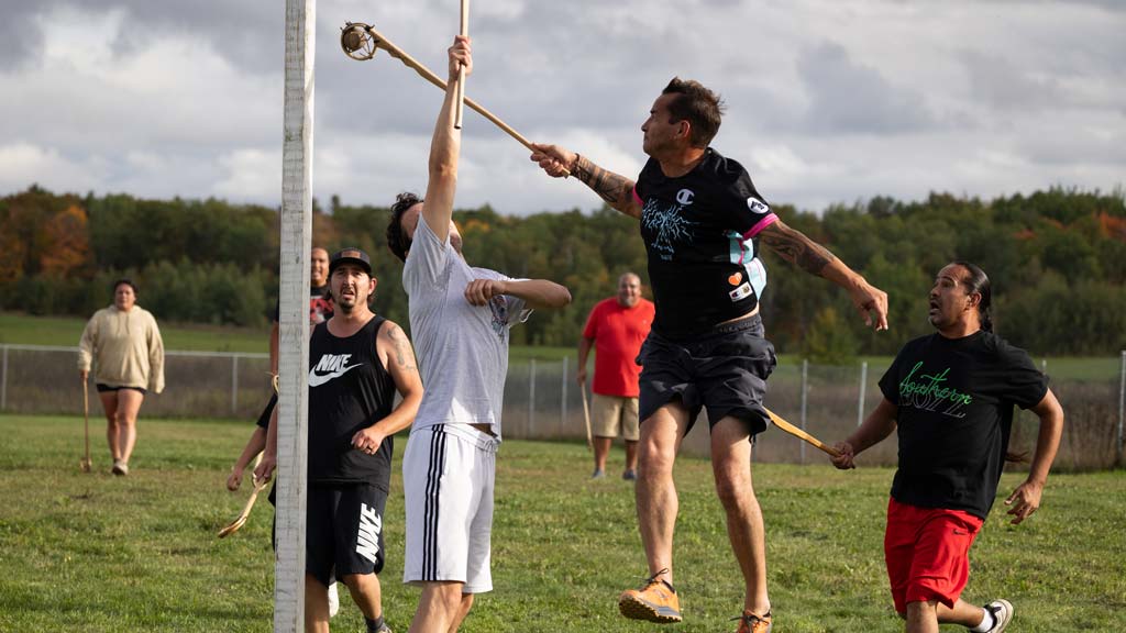 A group of people playing a game involving a small ball and long rackets with a netted cup on the end.