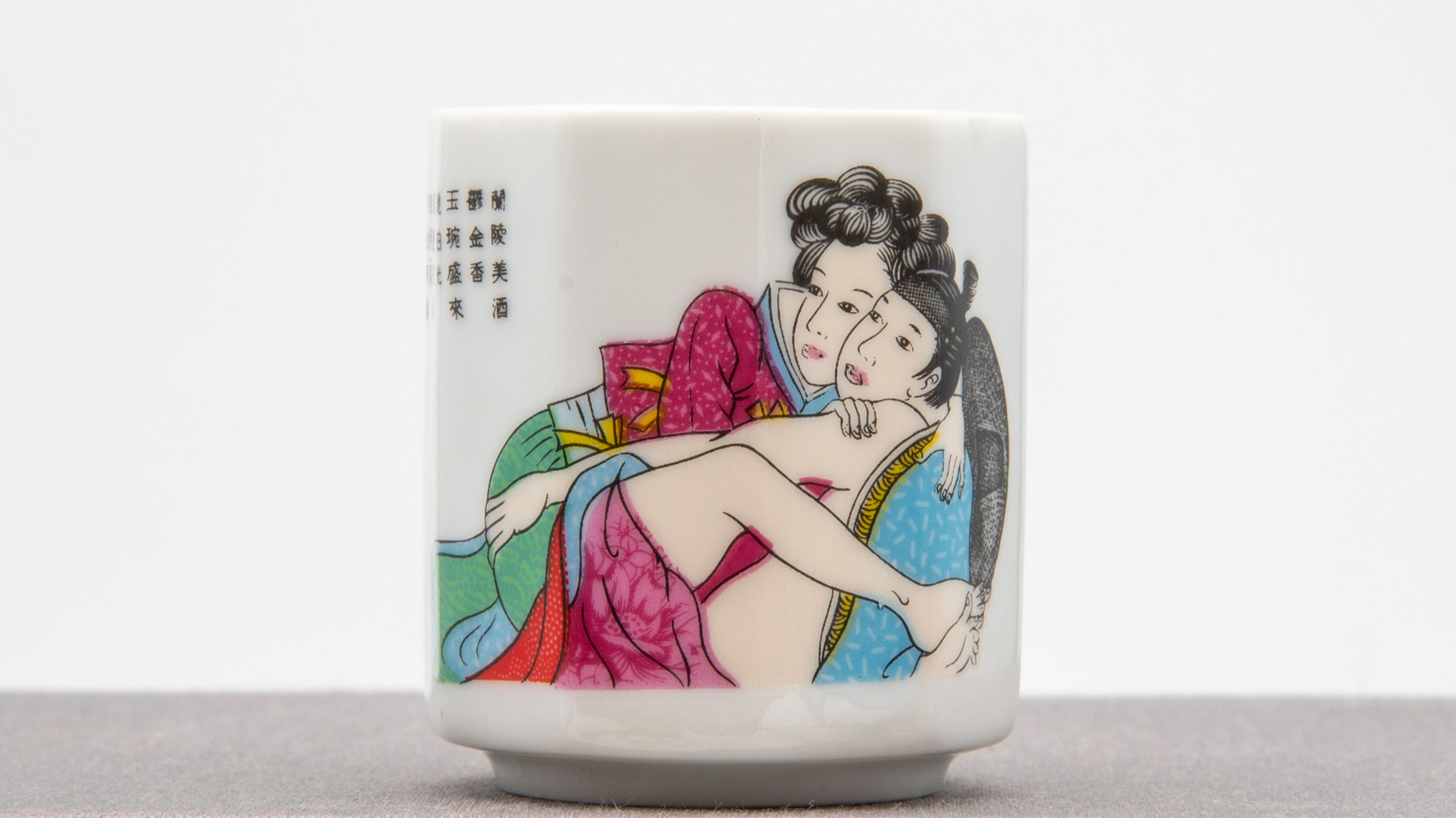 A japanese sake cup, with an image of a semi-undressed man and woman on it, looking to the side in the same direction.