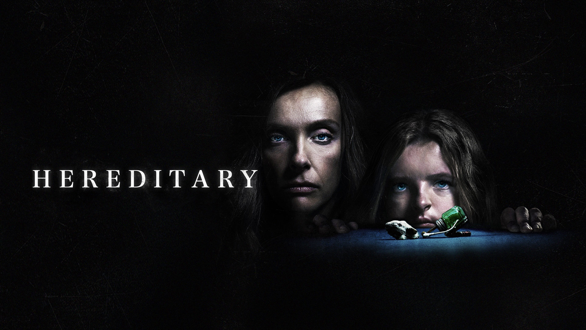 The poster of Hereditary. A woman and her child in a dark room, looking over a table at the viewer.