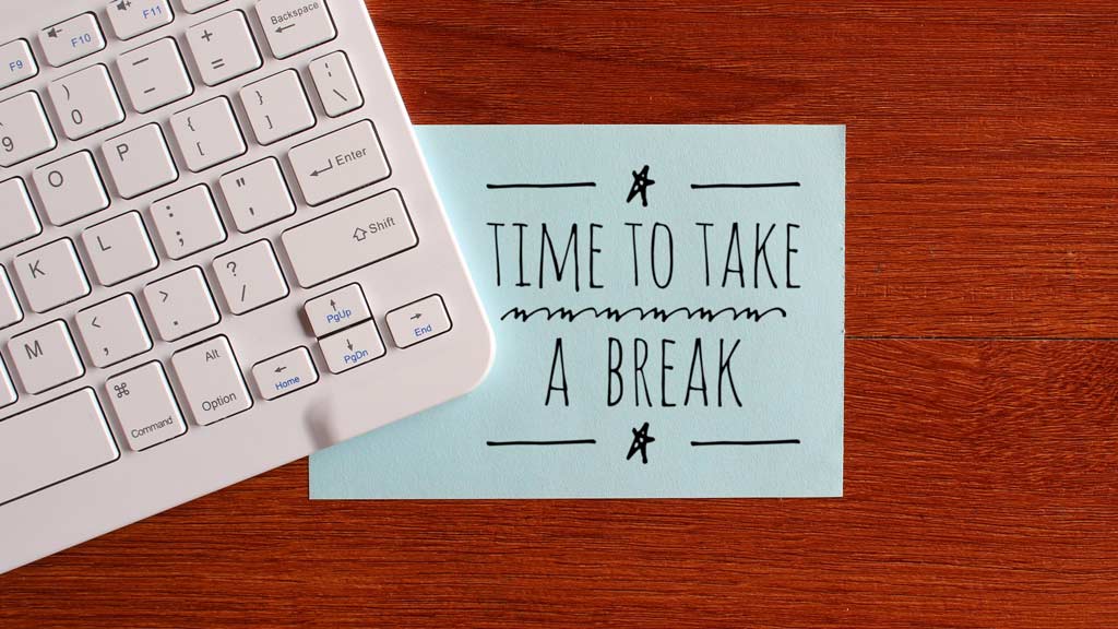A white keyboard overlapping a sticky note that says "time to take a break" on top of a desk