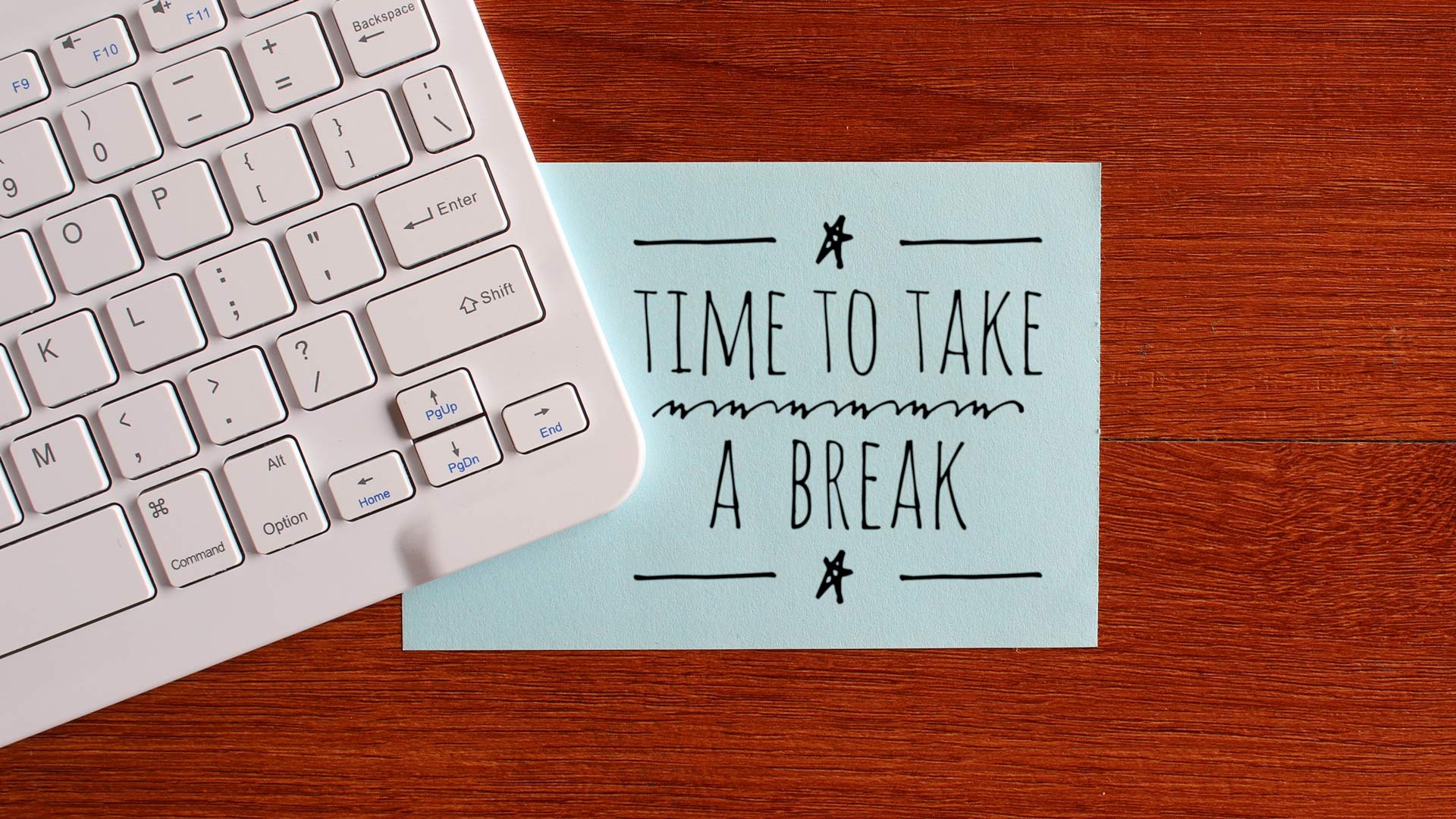 A white keyboard overlapping a sticky note that says "time to take a break" on top of a desk