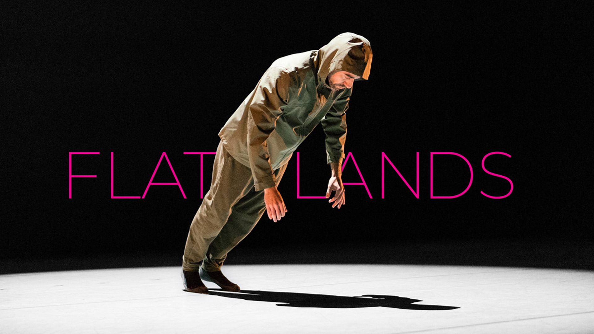 dancer wearing a hooded jacket and pants leaning forward over a spotlight in front of FLATLANDS text