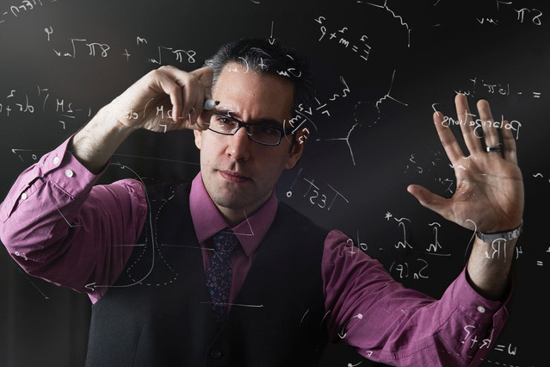 Man writing math equations on a clear whiteboard