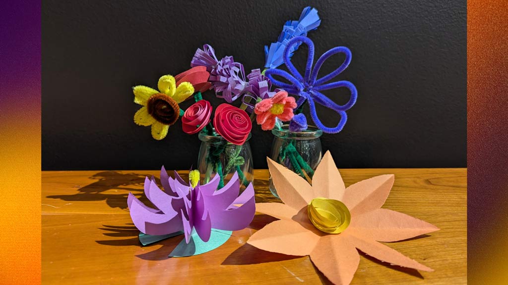 A picture of a variety of flowers made of paper, and pipe cleaners on top of a wooden table top.