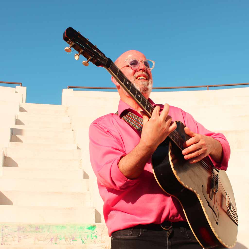 A press photo of a person on the steps of a building playing a guitar.
