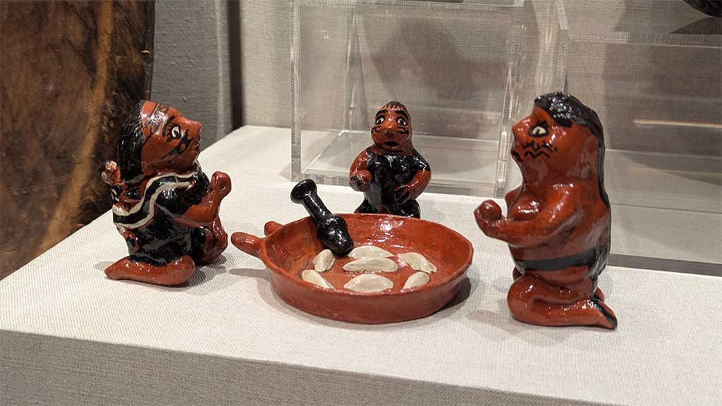 three ceramic figures kneeling around a ceramic figure of a wide-bottom dish of fruit with a masher