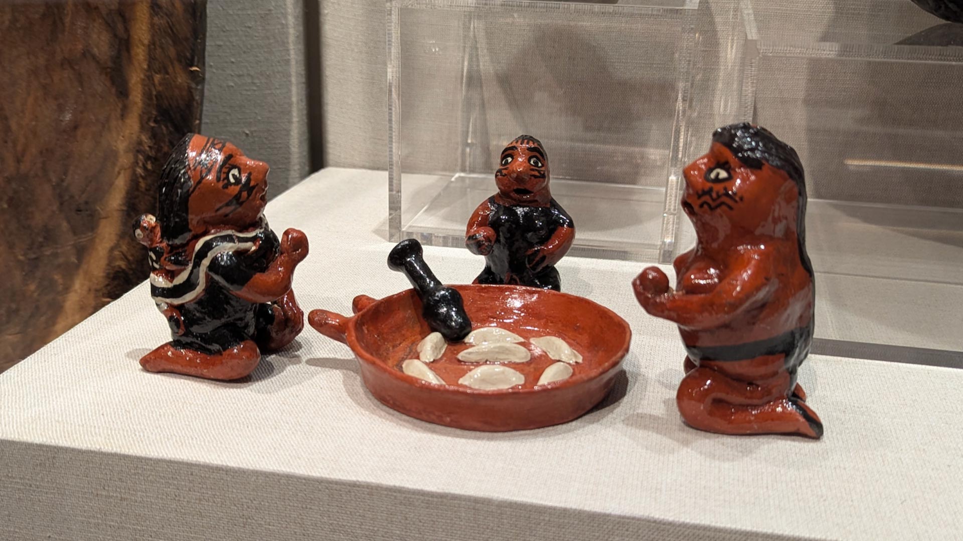 three ceramic figures kneeling around a ceramic figure of a wide-bottom dish of fruit with a masher