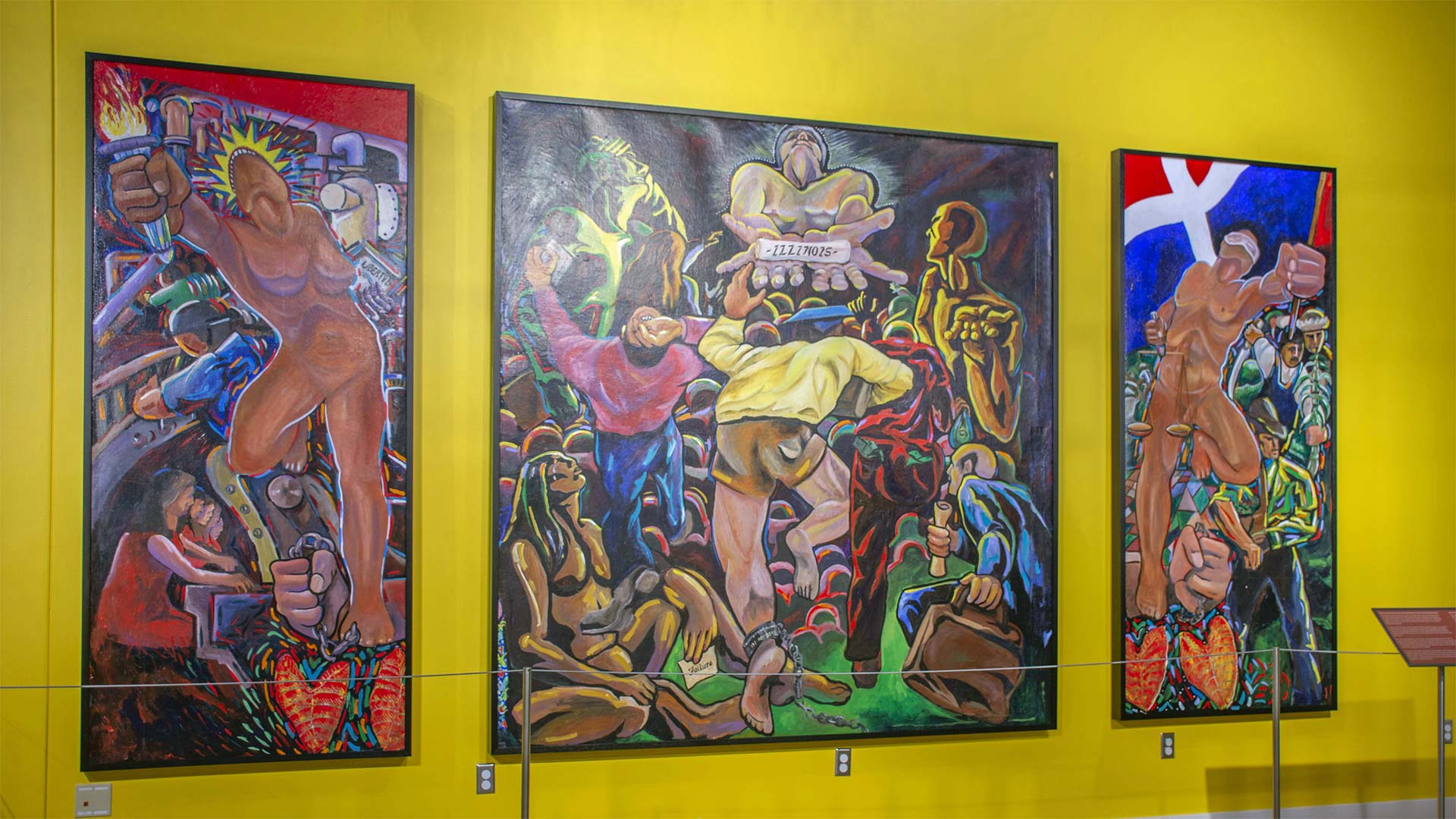 An exhibit wall with three art panels with people working an in empowerment poses