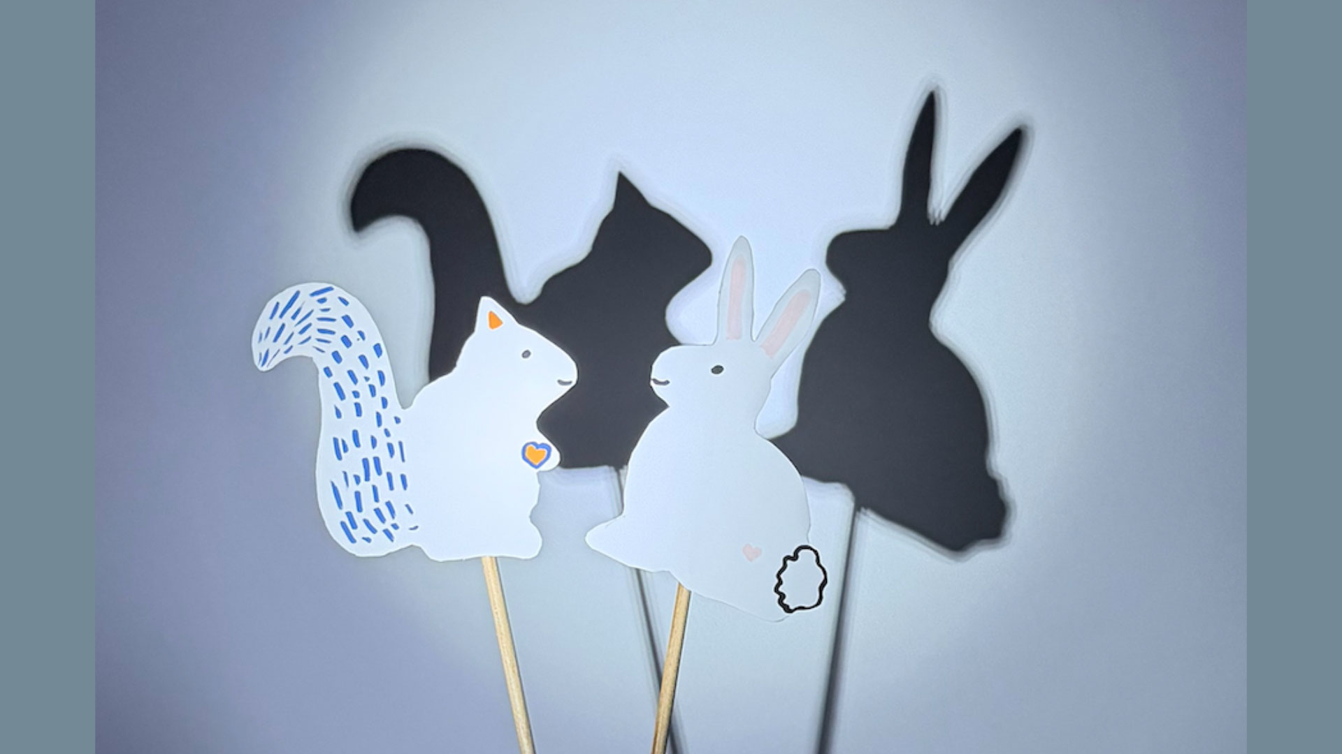 A squirrel and rabbit paper puppet cutout illuminated and casting shadows on the wall.