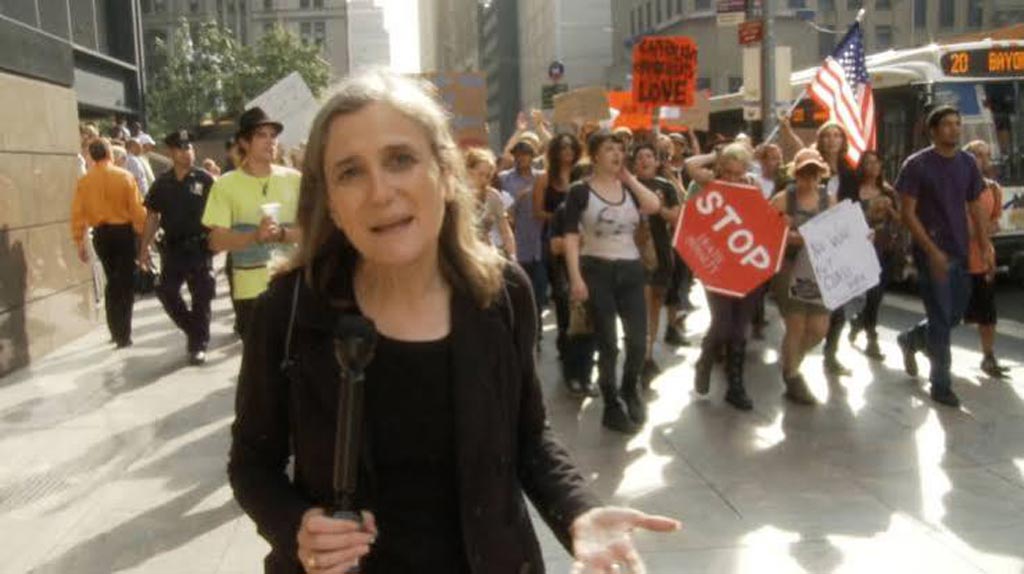 View from a news camera showing a reporter walking with a group of protesters on the city streets