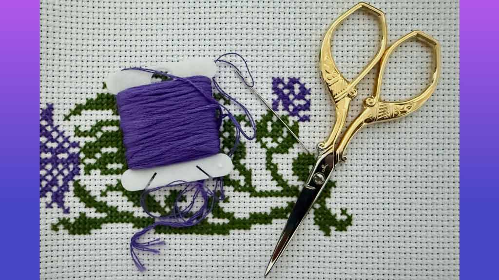 Stitching scissors and yarn laid over a woven cloth with a purple flower