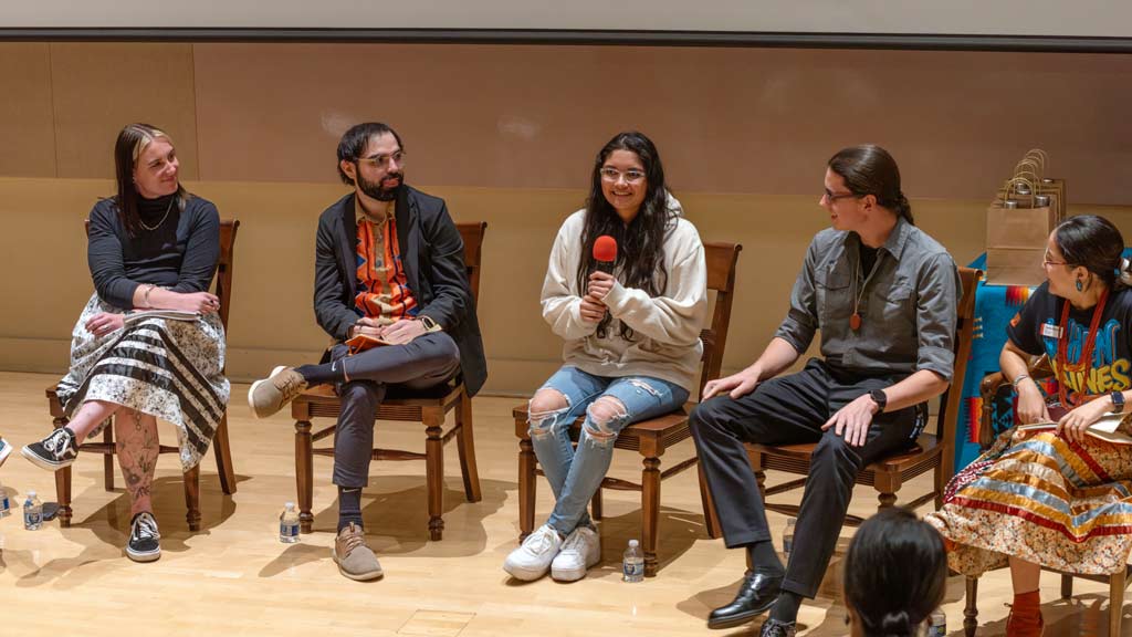 A panel of people sitting in chairs while speaking to an audience