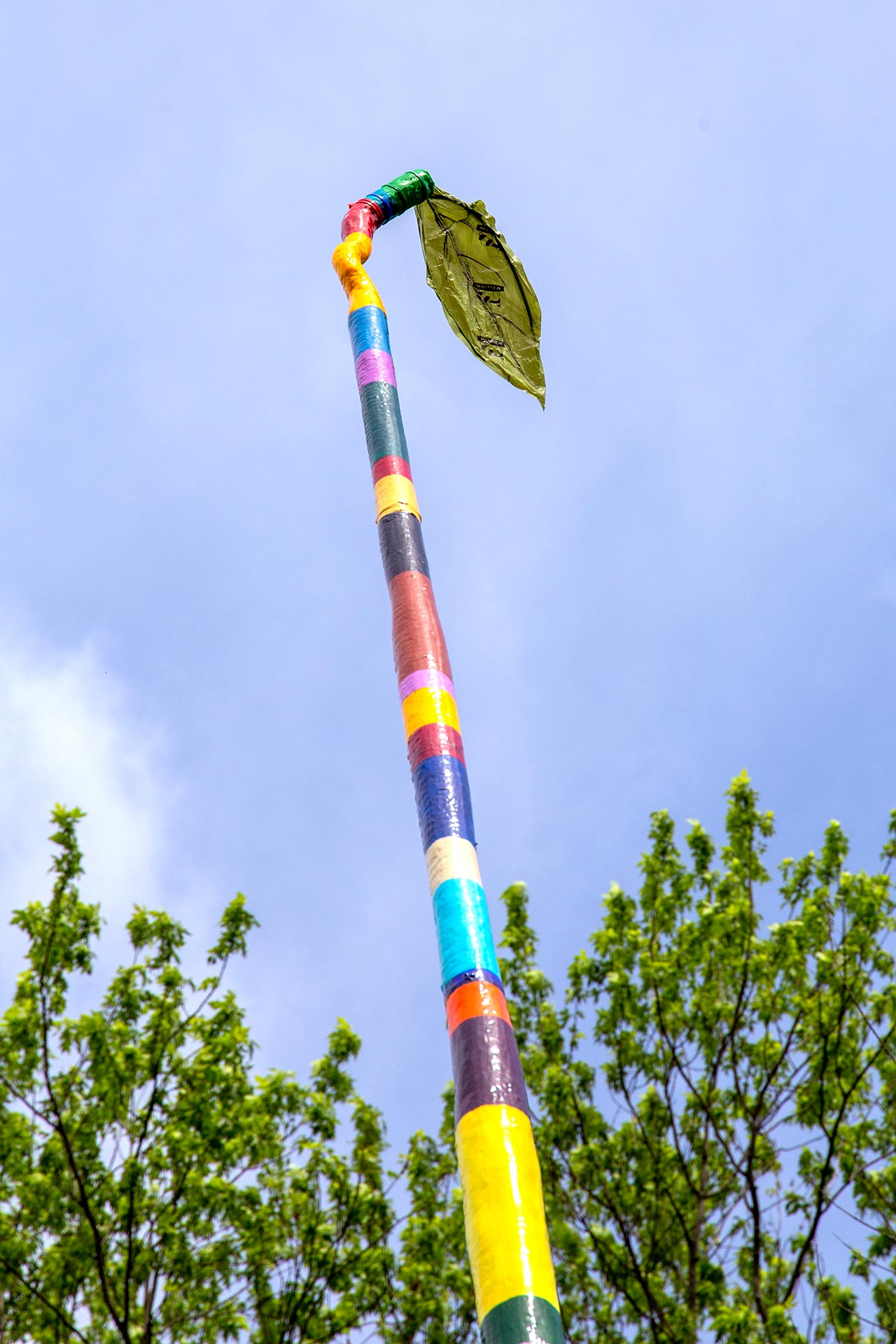 A tall stick with colorful stipes that has a plastic-made leaf on the top