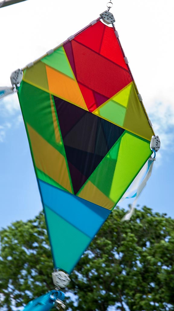 A kite with geometric rainbow-colored patterns being framed against the sky