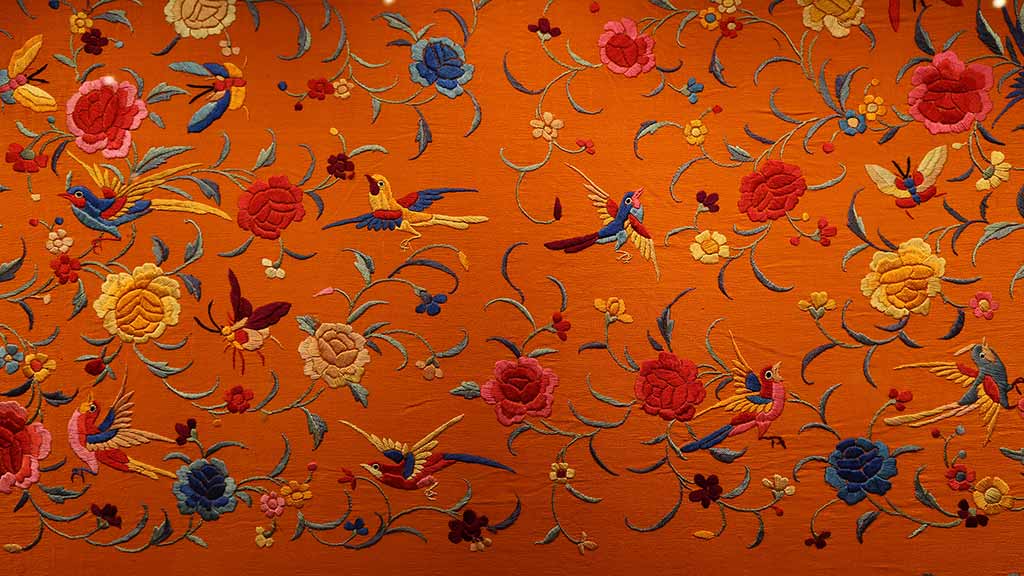 orange textile with embroidered flowers and birds