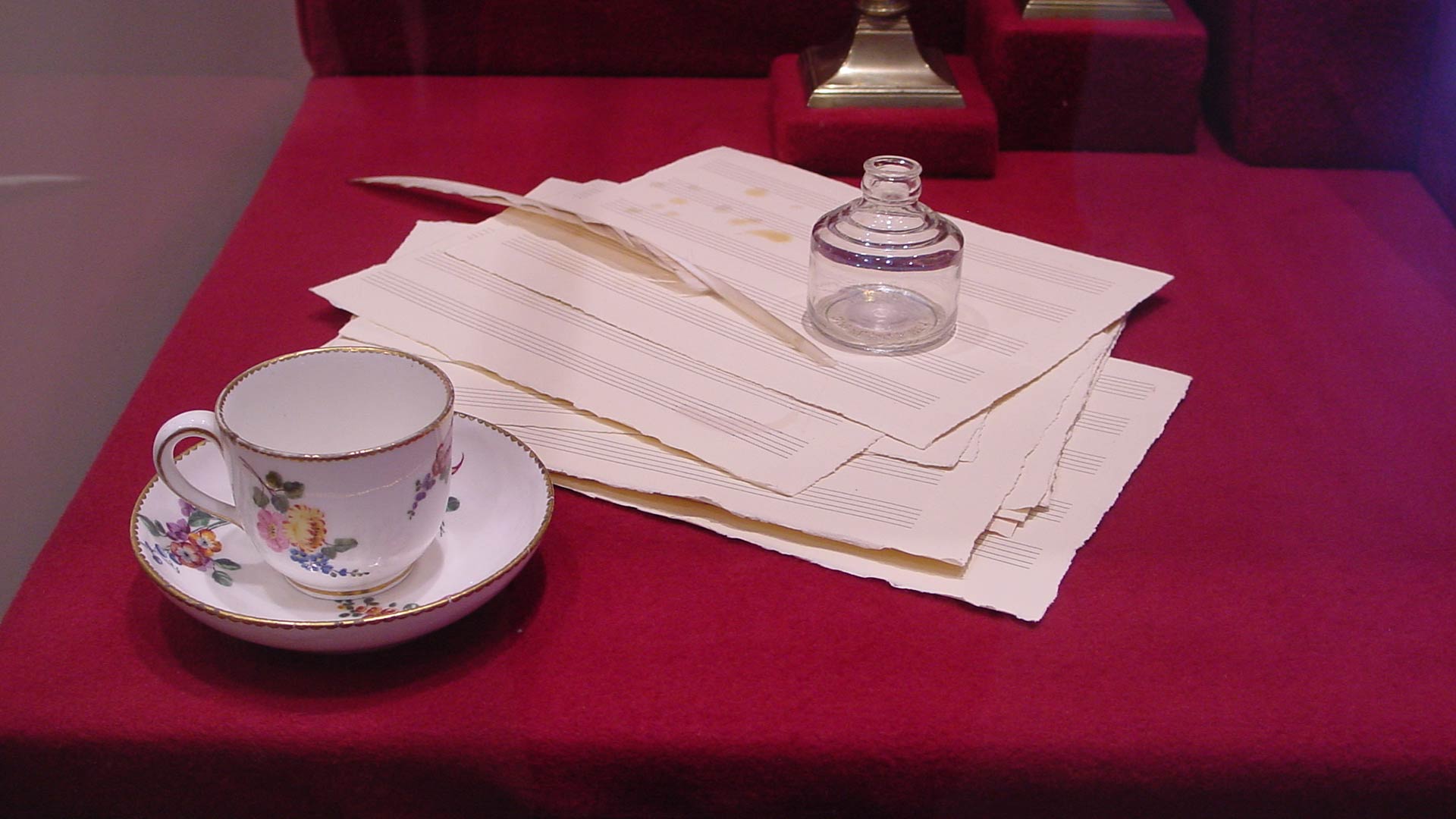 closeup of tea set, glass bottle, feather pen and music score sheet