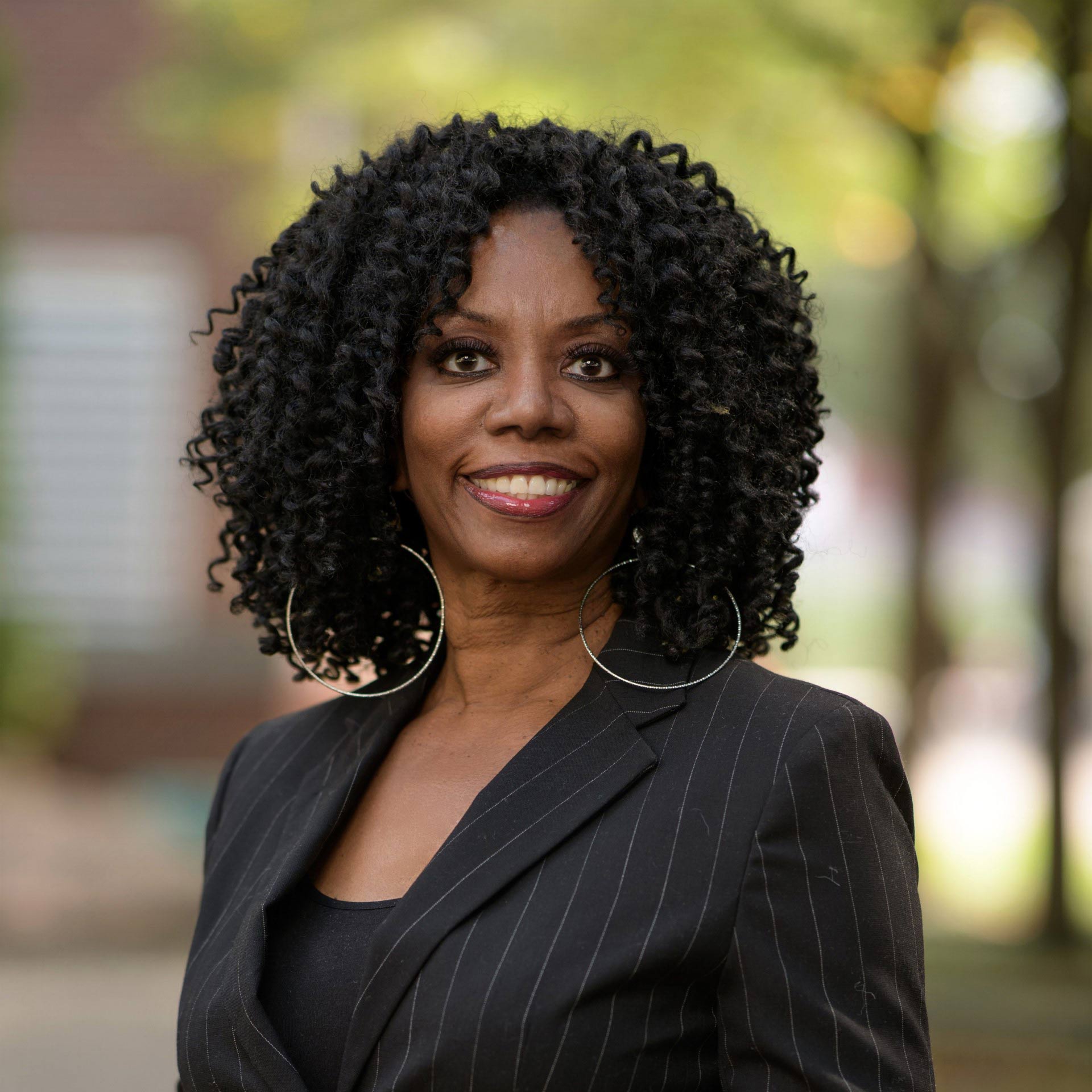 headshot of a Black woman wearing a black striped blazer outdoors