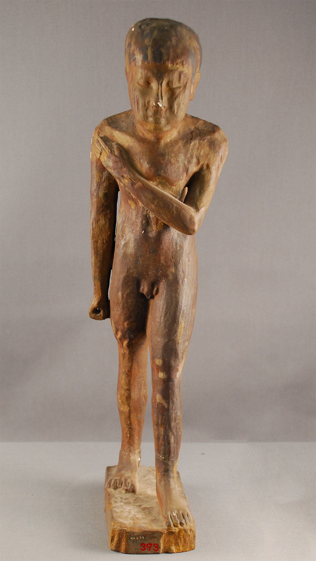 figurine of a man with a curved spine, showing the man striding with his left leg, emphasizing the curved spine with his right hand