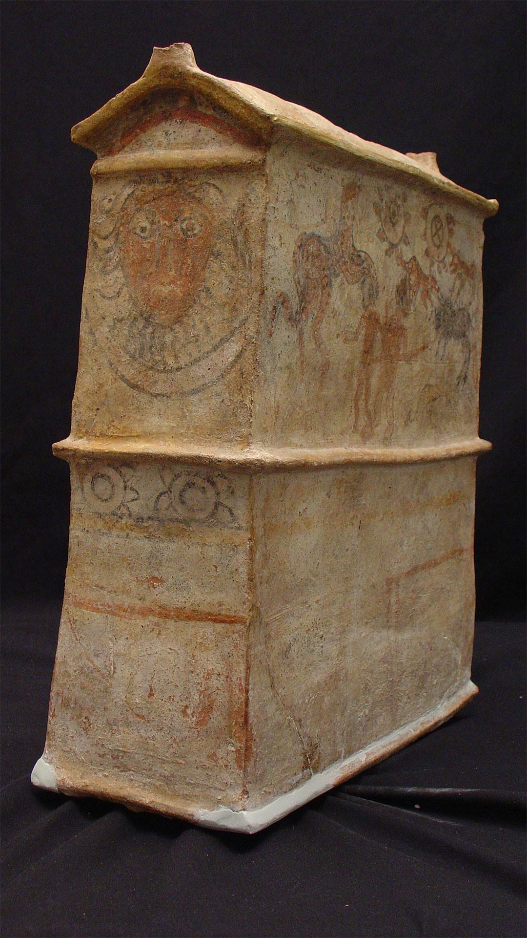 terracotta sarcophagus with a gorgon face painted on it, as well as a pair of humans surrounded by animals painted on the side