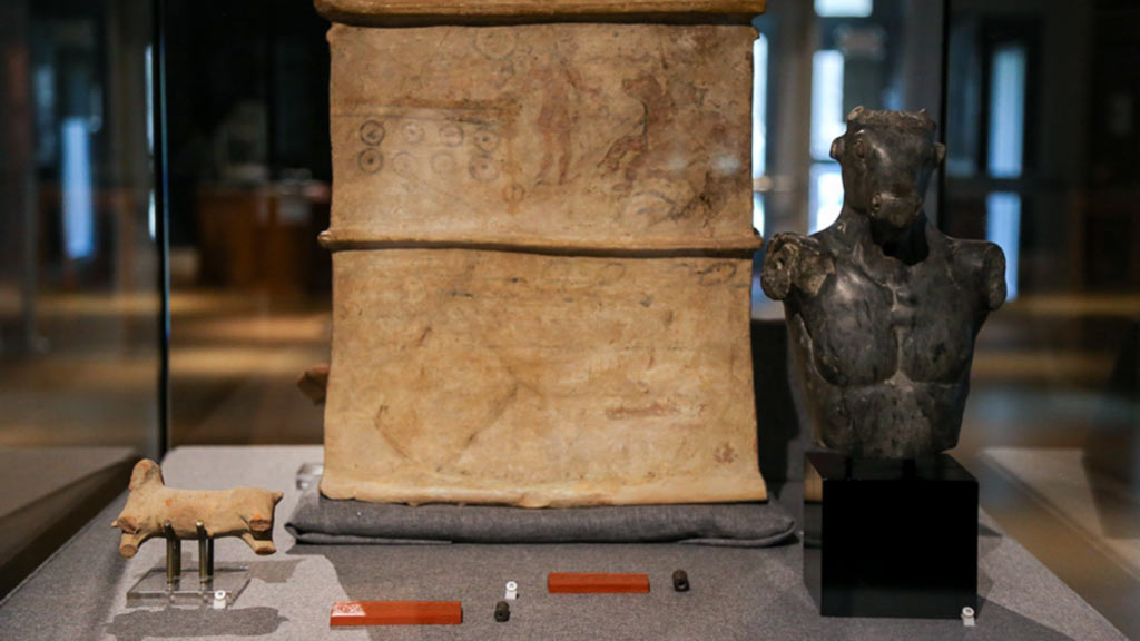 case shot including a terracotta sarcophagus, a minotaur statue, and cylinder seals with bull hybrids
