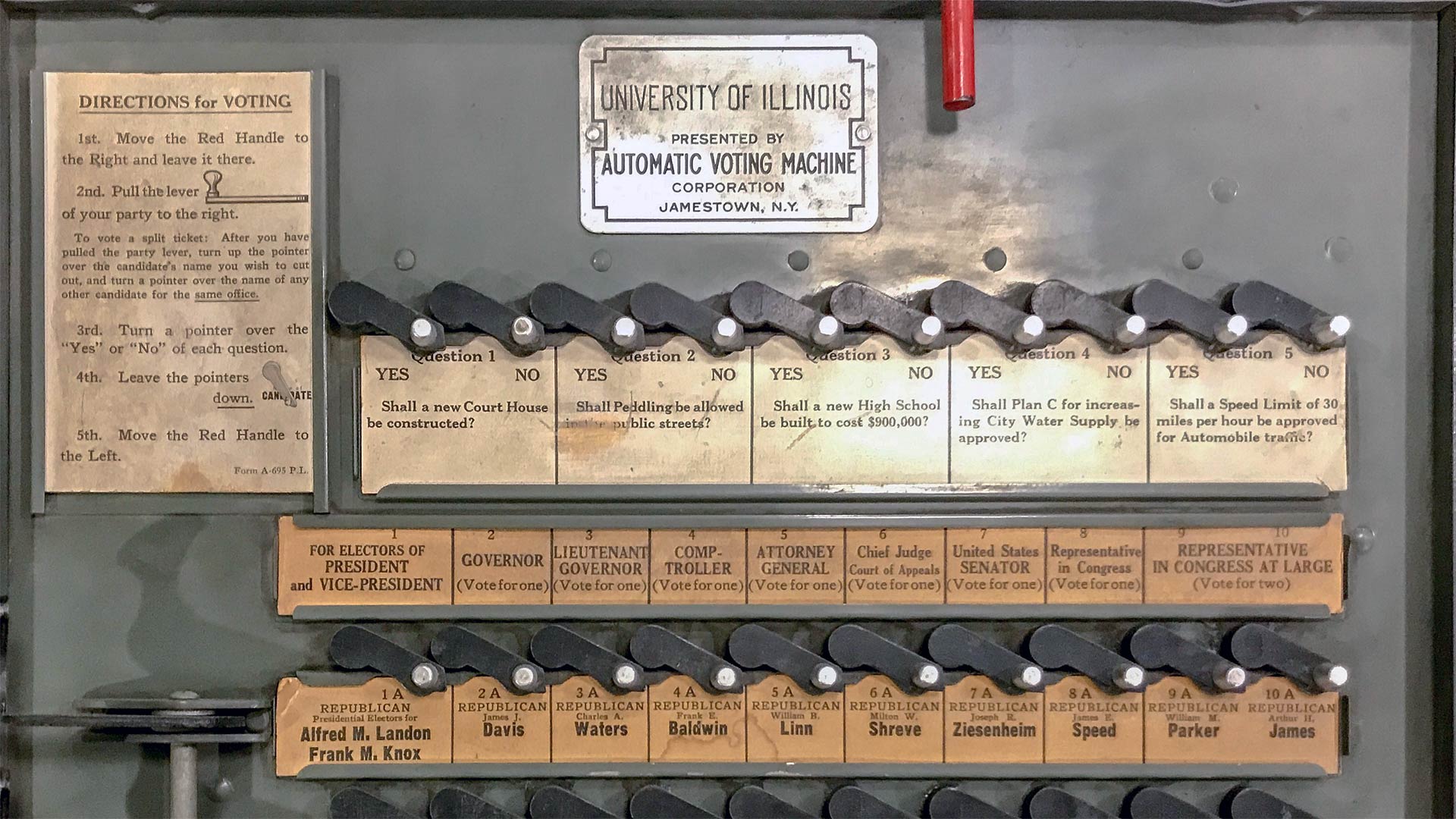Photo of an old mechanical voting machine with a University of Illinois plaque and visible referenda and candidates
