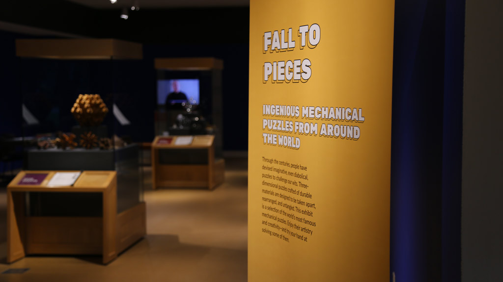 the exhibit banner that reads: 'fall to pieces: ingenious mechanical puzzles from around the world' with additional text