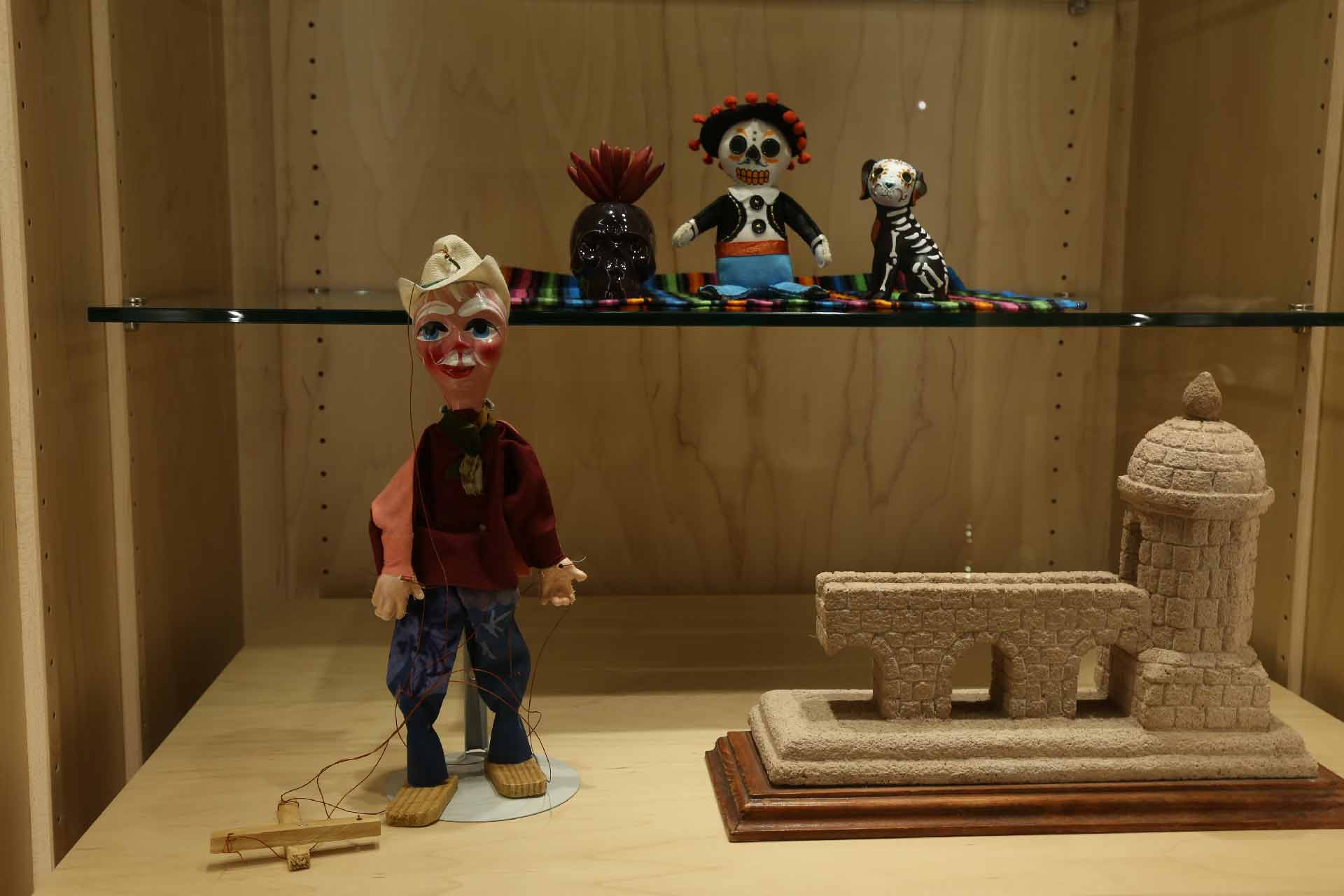 the skull, figure and dog sitting on the color mat sit on a platform while a puppet doll and a small piece of a building sculpture are underneath