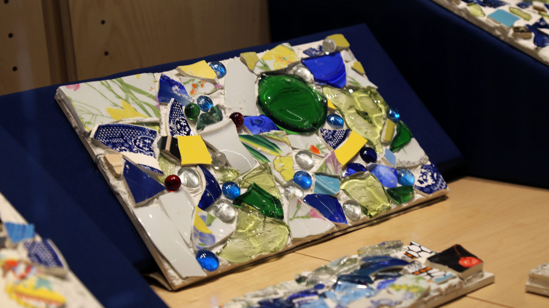 a close-up of one of the mosaics in the right case featuring broken plates, glass beads, and other materials