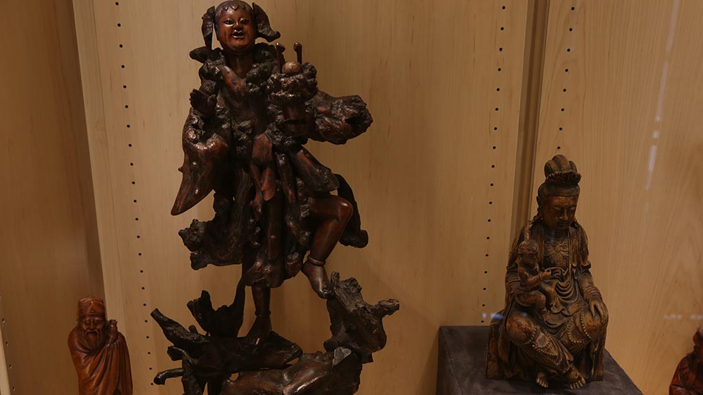 a close-up of two more sculptures, with the bigger focused one depicting a person standing on top of branches and someone holding on to them