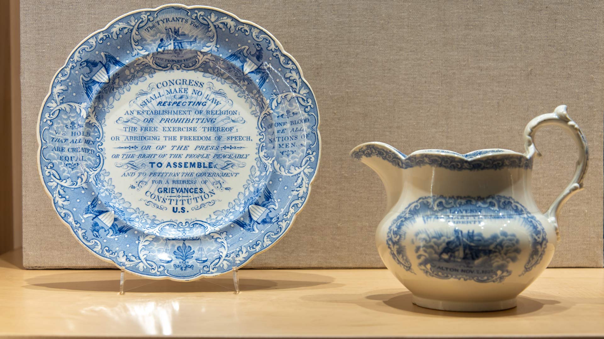 blue and white china plate with a decorative motif listing the first amendment to the US Constitution and a matching tea cup that says liberty.
